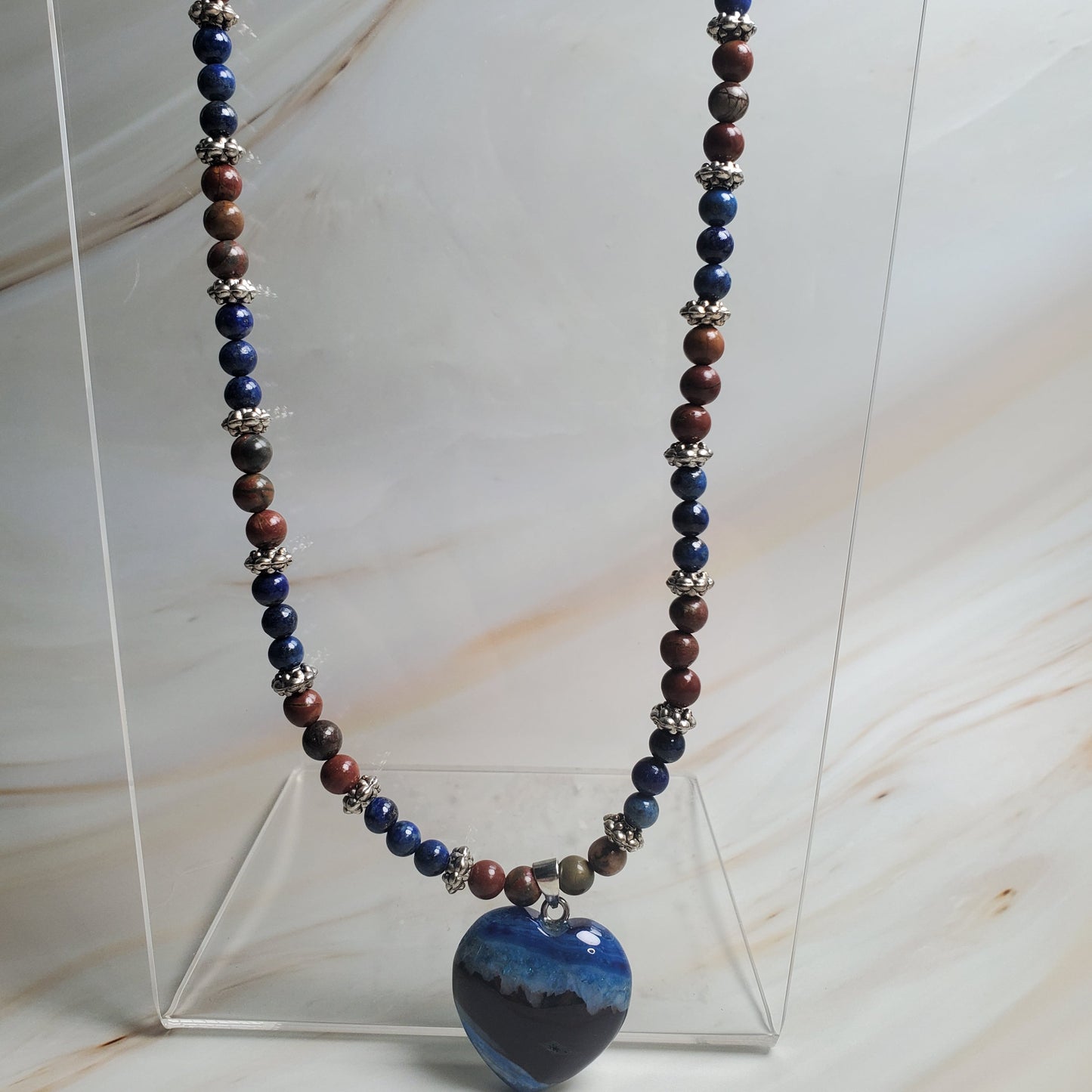Necklace with multicolored beads on a clear stand against a marble background