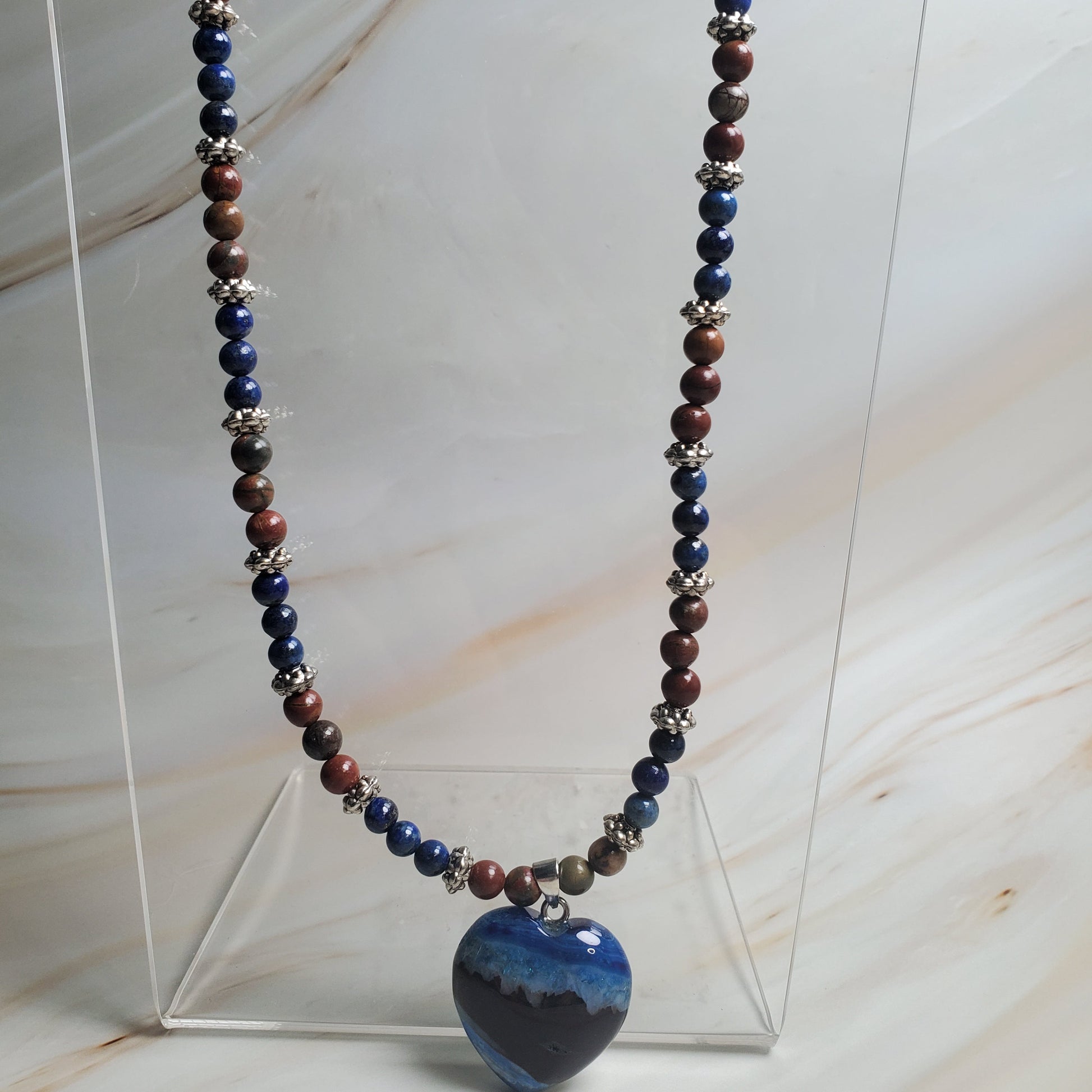 Necklace with multicolored beads on a clear stand against a marble background