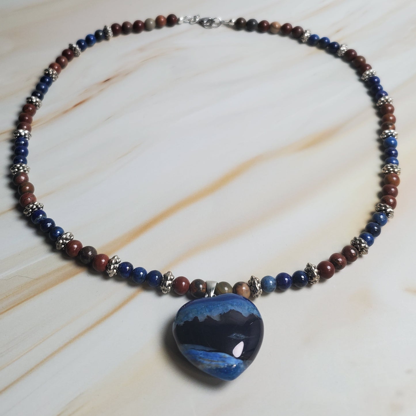 Beaded necklace with a large blue stone pendant on a light wood surface