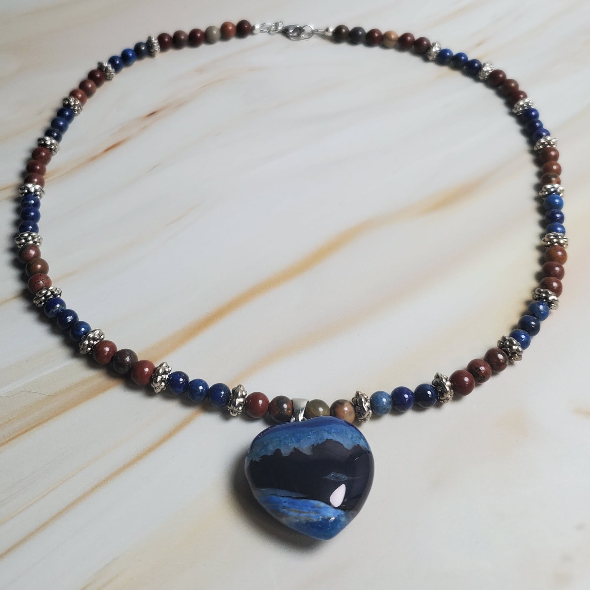 Beaded necklace with a large blue stone pendant on a light wood surface