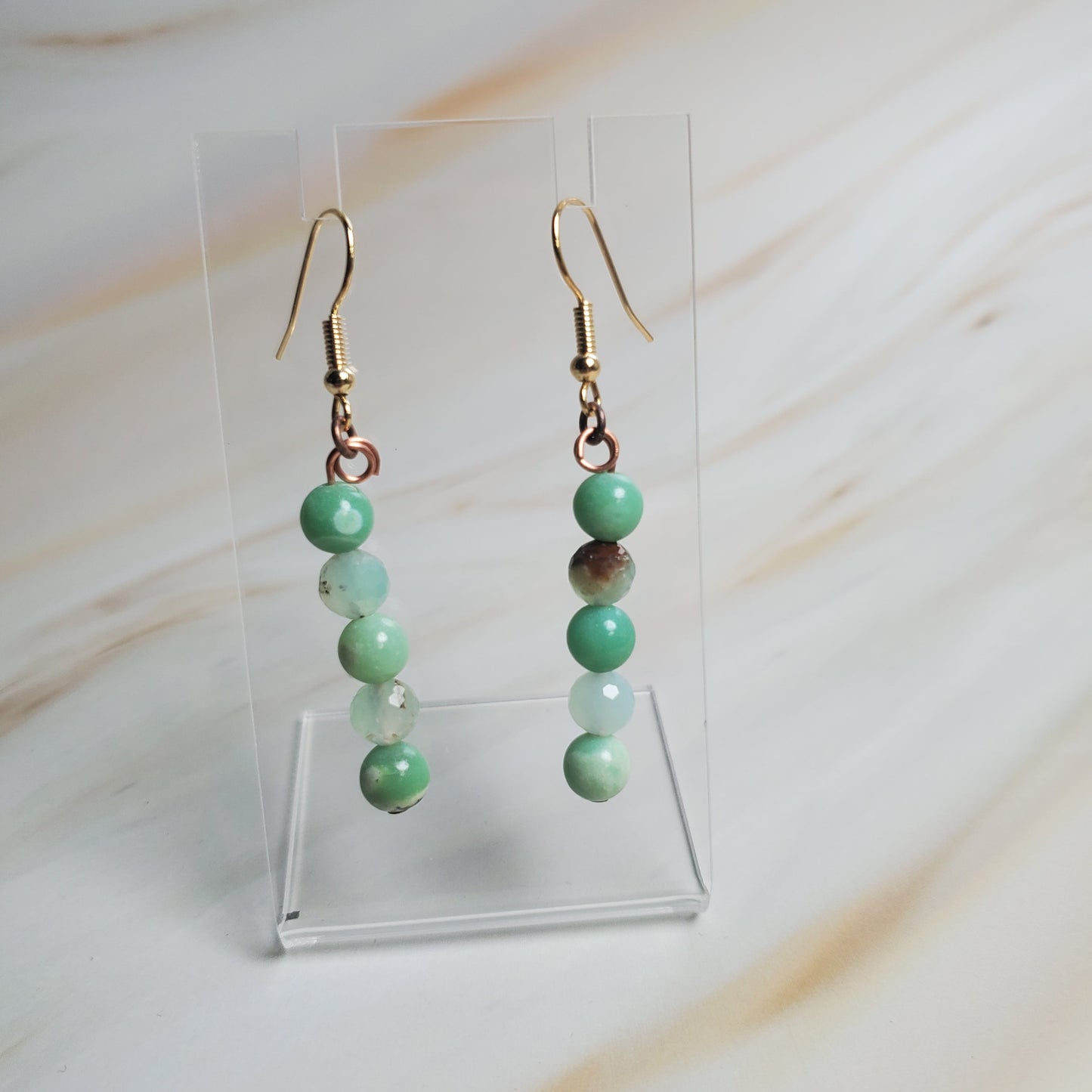 Green beaded earrings on a clear stand against a light background