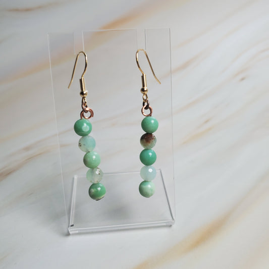 Green beaded earrings on a clear stand against a light background