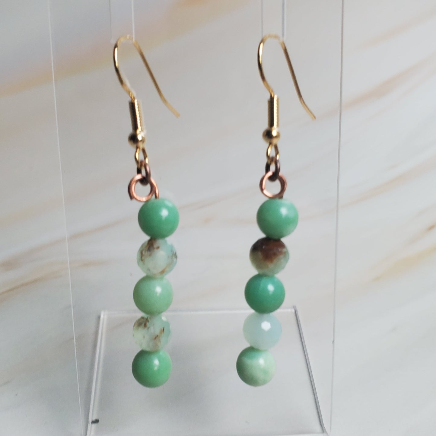 Green beaded earrings on a clear stand against a light background