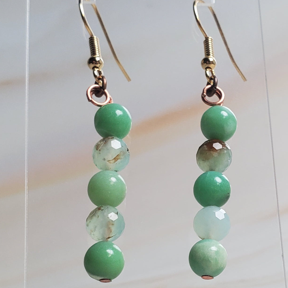 Green beaded earrings on a clear stand against a marble background