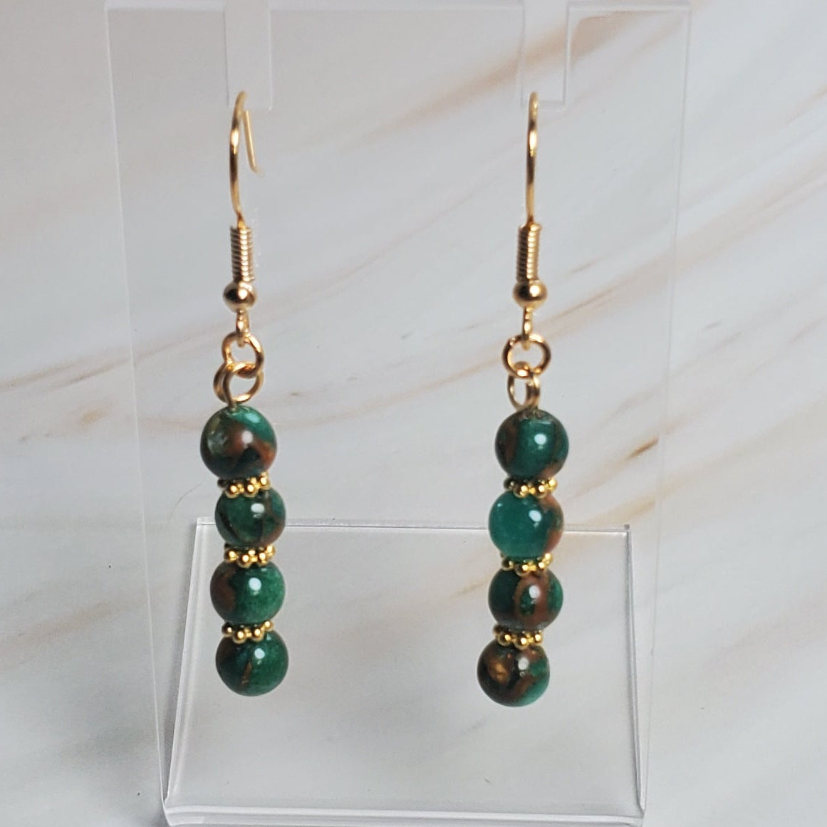 Pair of earrings on a clear stand against a marble background
