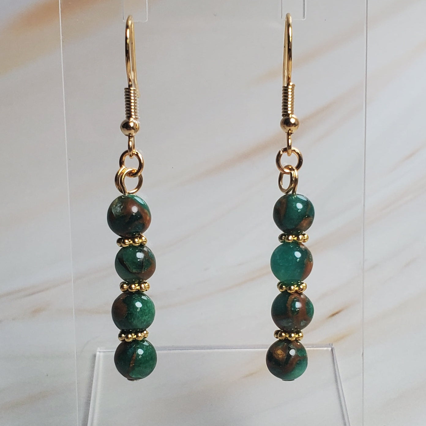 Pair of green beaded earrings on a clear stand against a marble background