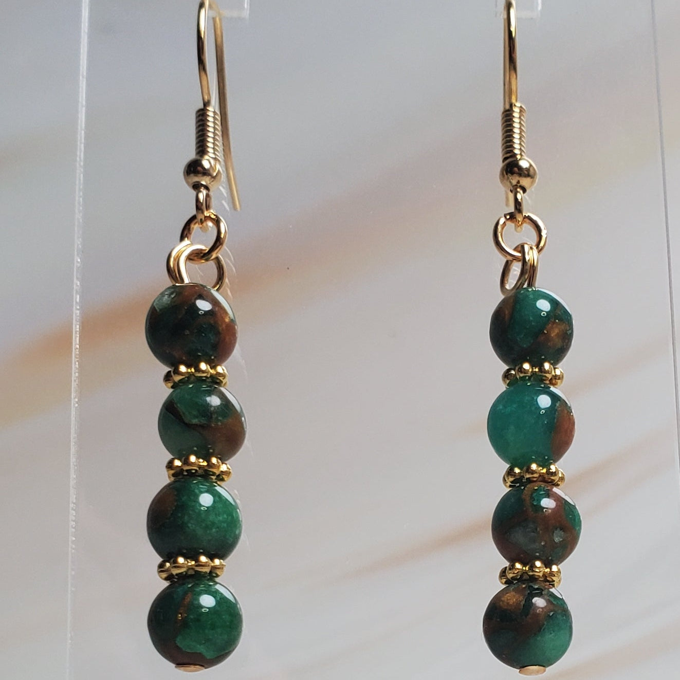 Green beaded earrings on a clear stand against a light wood background