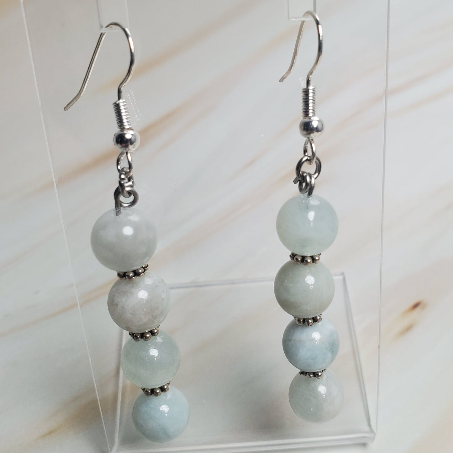 Pair of earrings with light blue beads on a clear stand against a neutral background