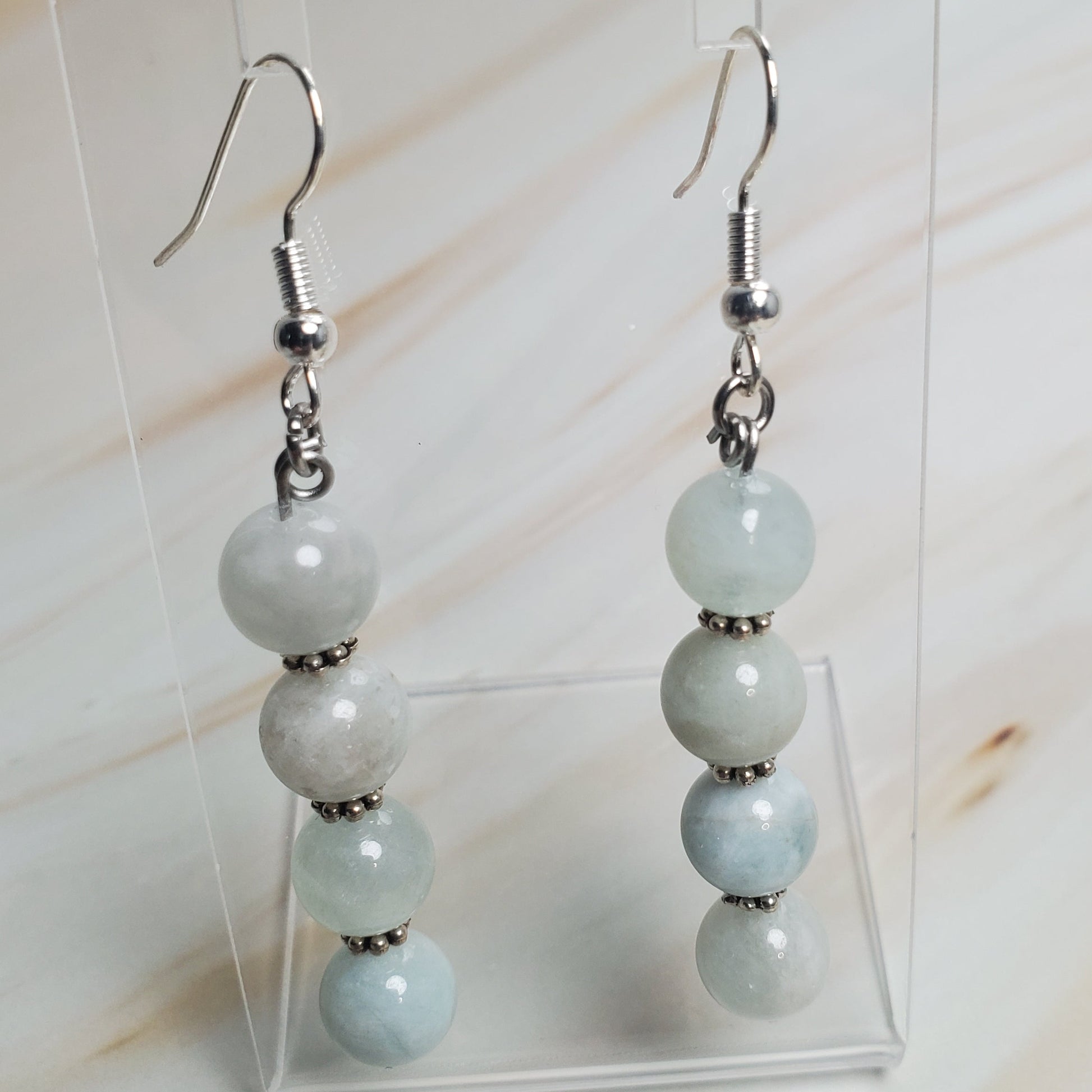 Pair of earrings with light blue beads on a clear stand against a neutral background