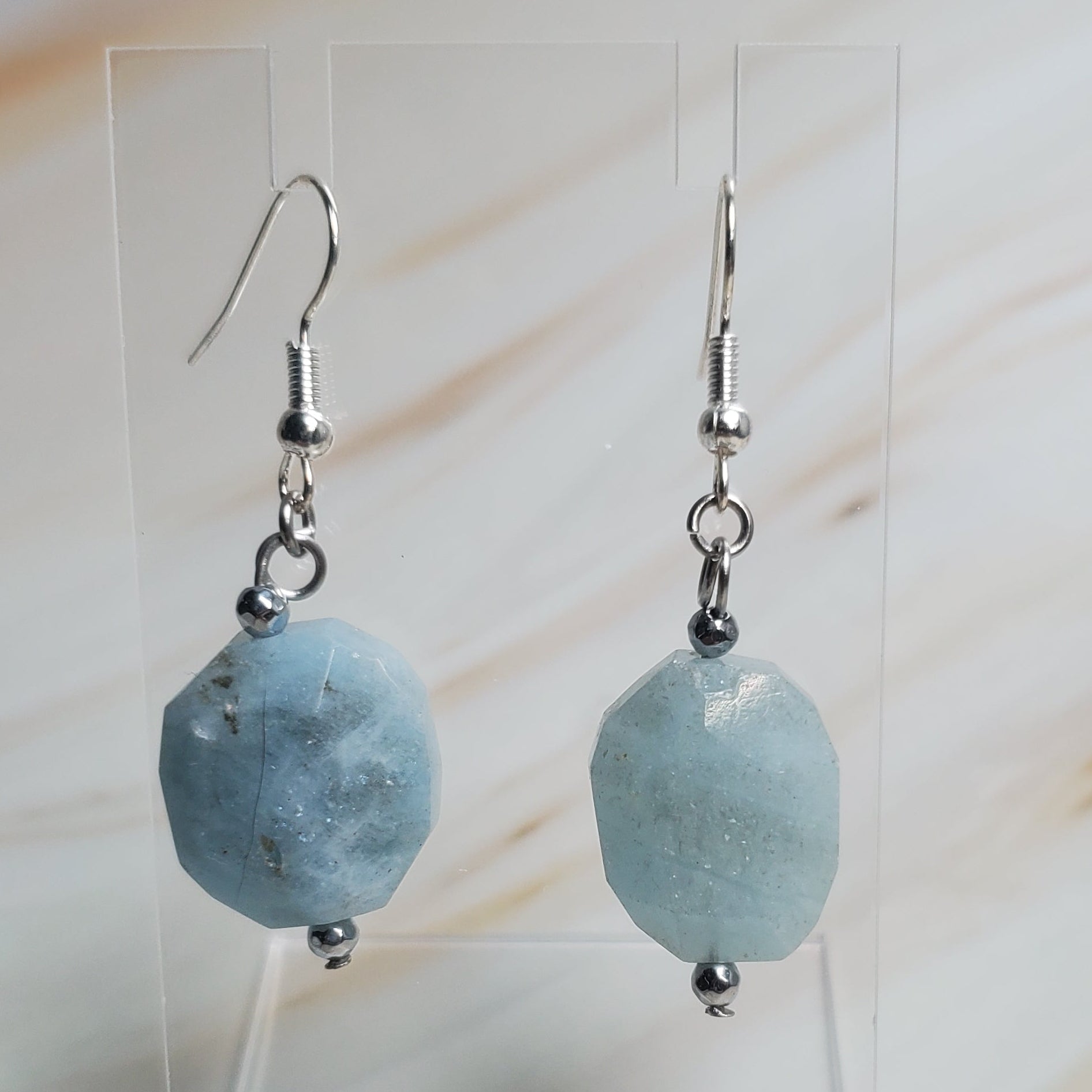 Pair of earrings with blue beads on a clear stand against a marble background