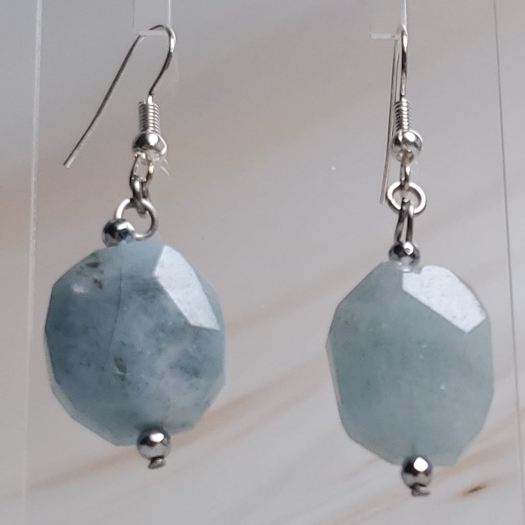 Pair of earrings on a clear stand against a marble background