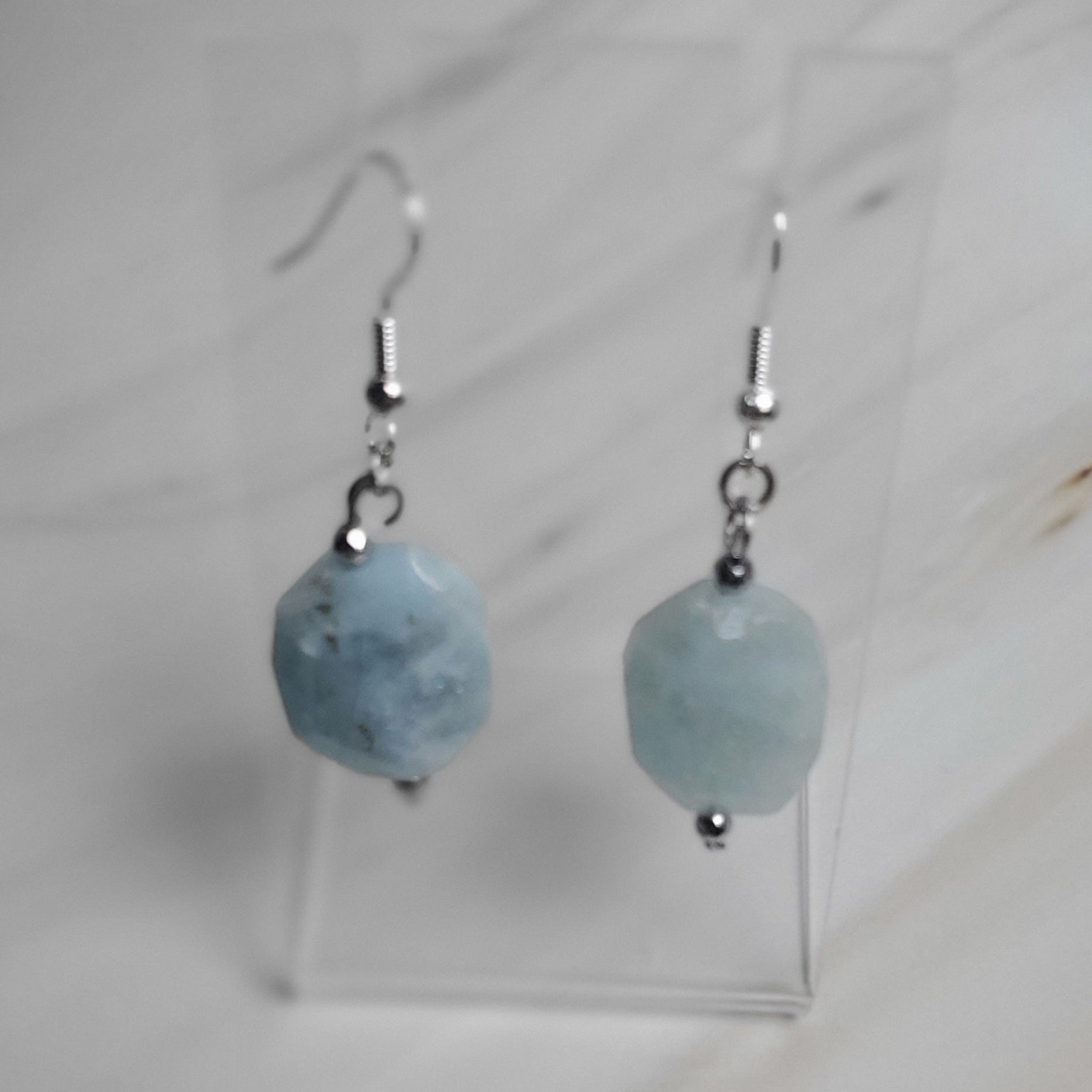 Pair of earrings with blue spherical beads on a clear stand against a light background