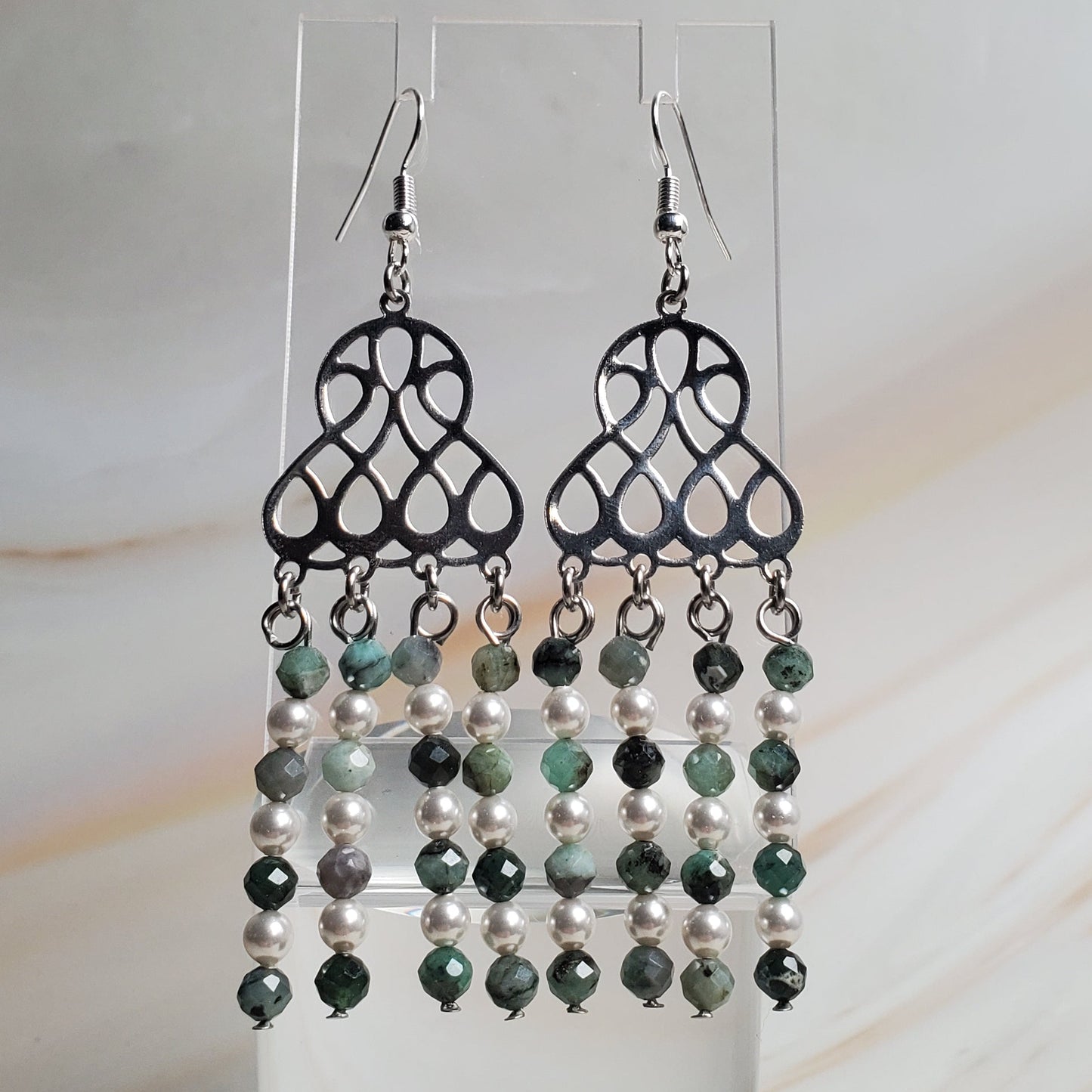 Pair of beaded earrings on a clear stand against a marble background