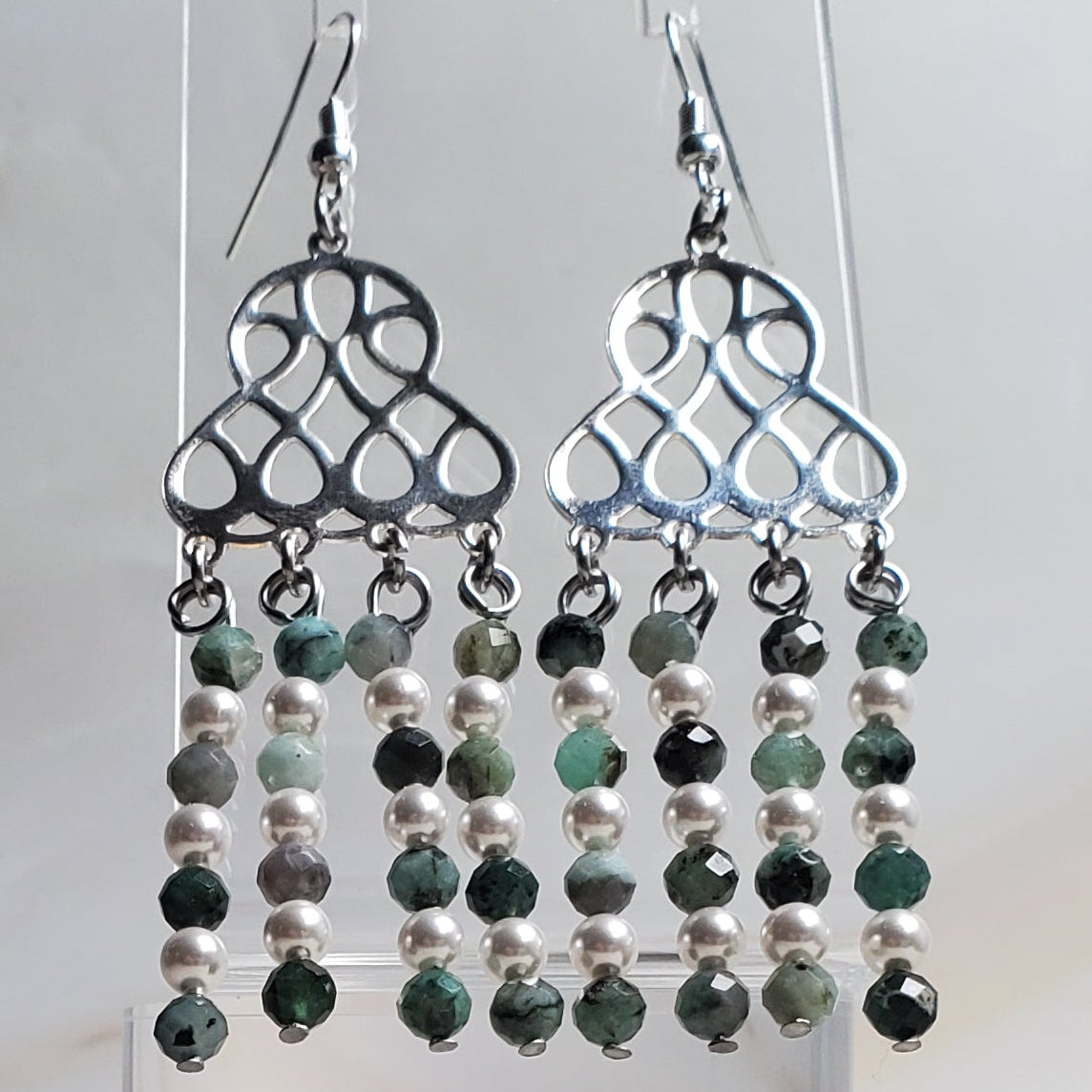 Earrings with green beads in a clear glass holder on a marble background