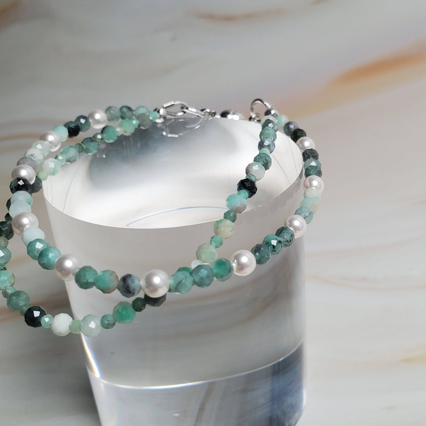 Stacked beaded bracelet on a cylindrical silver holder against a marble background