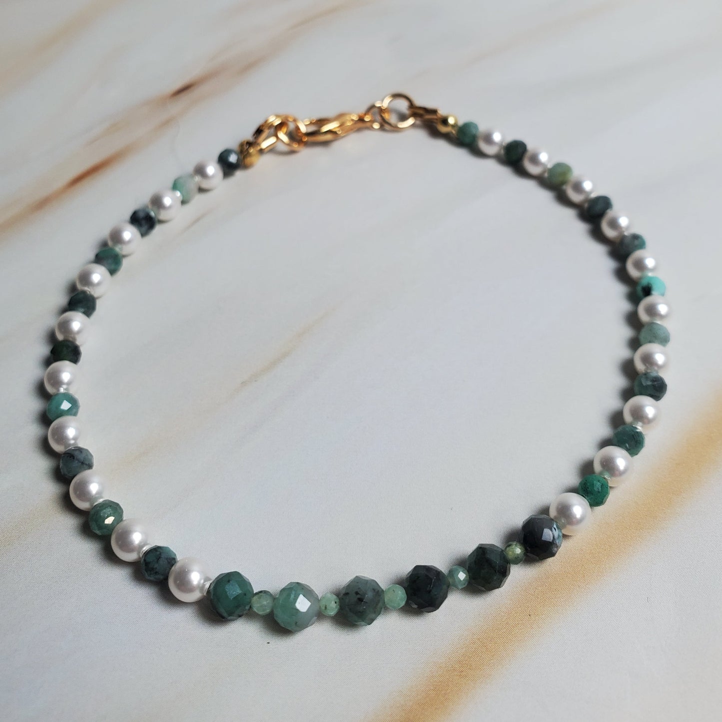 Beaded bracelet with green and white beads on a marble surface