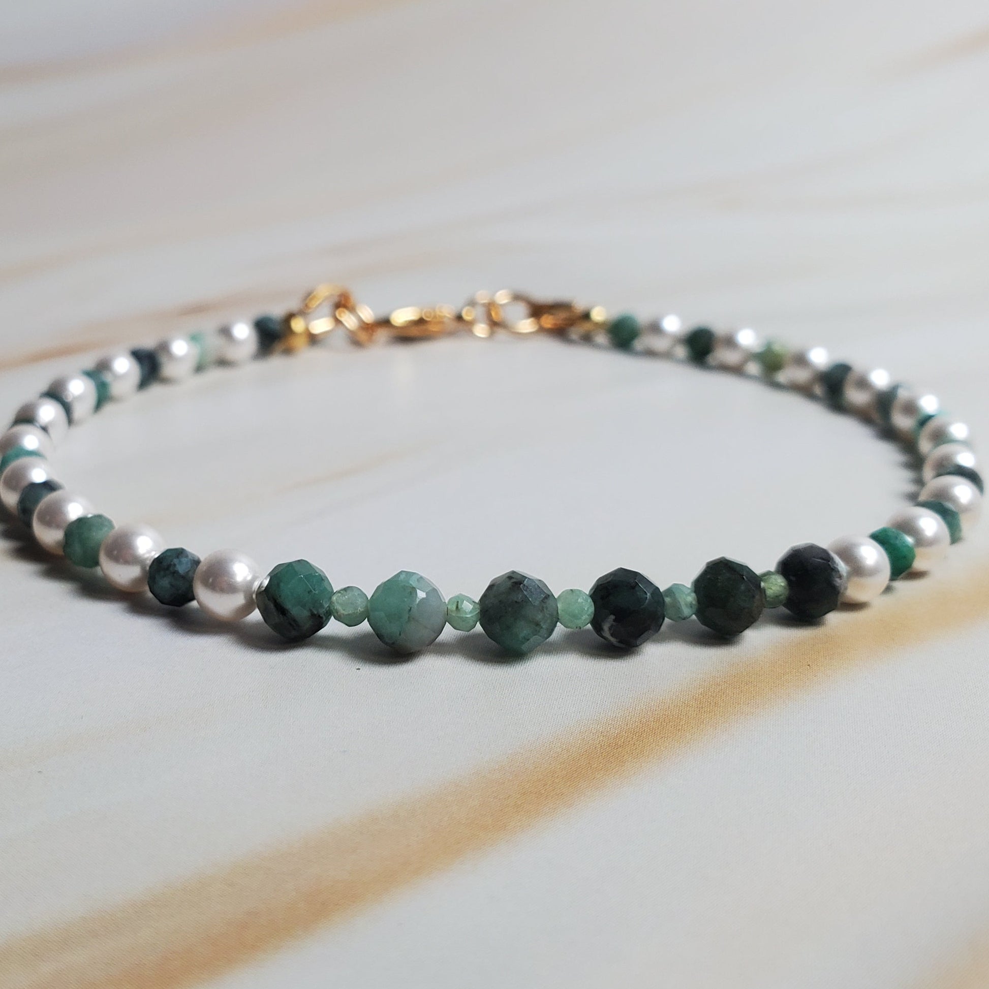 Beaded bracelet with green and silver beads on a light wooden surface