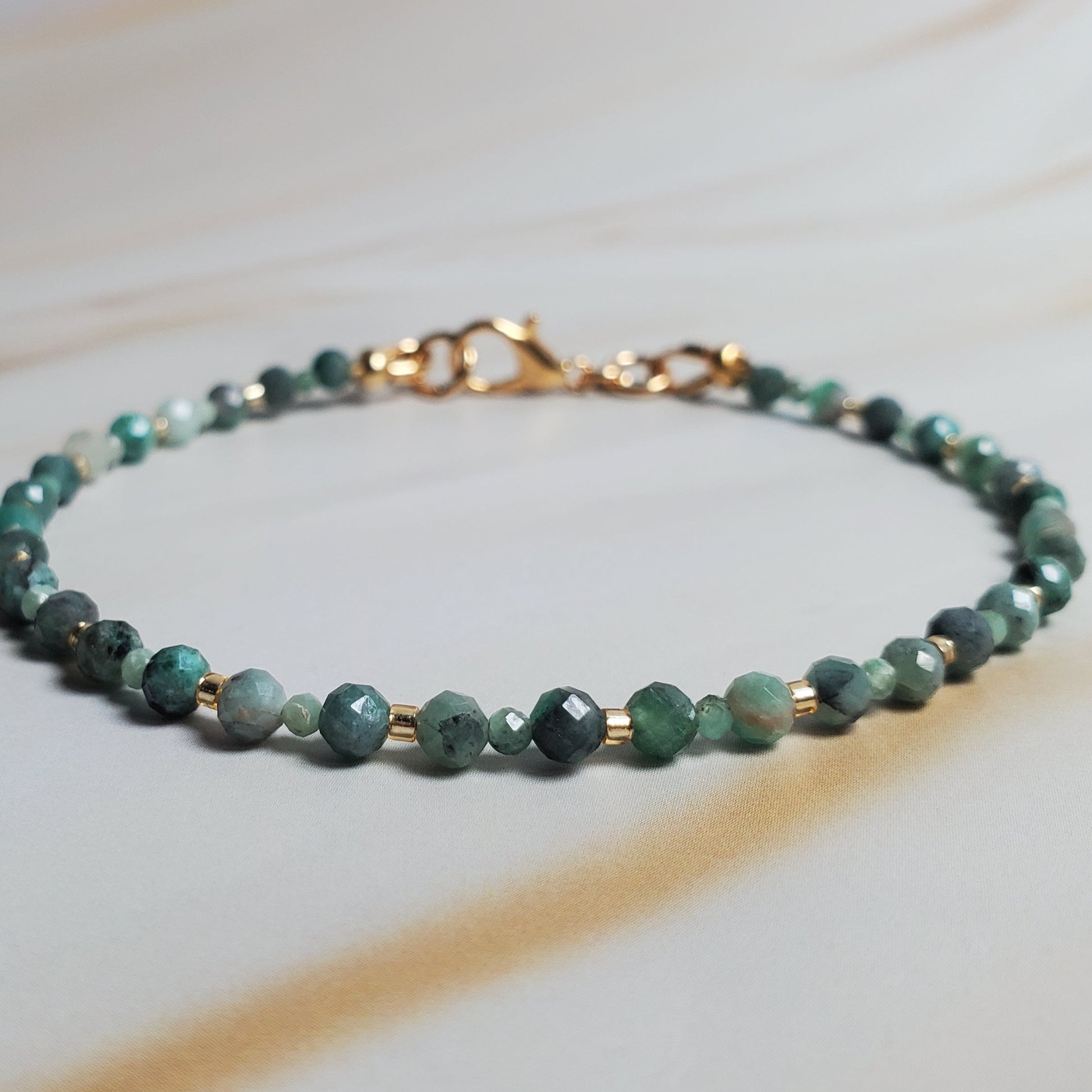 Green beaded bracelet with gold clasp on a light wooden surface