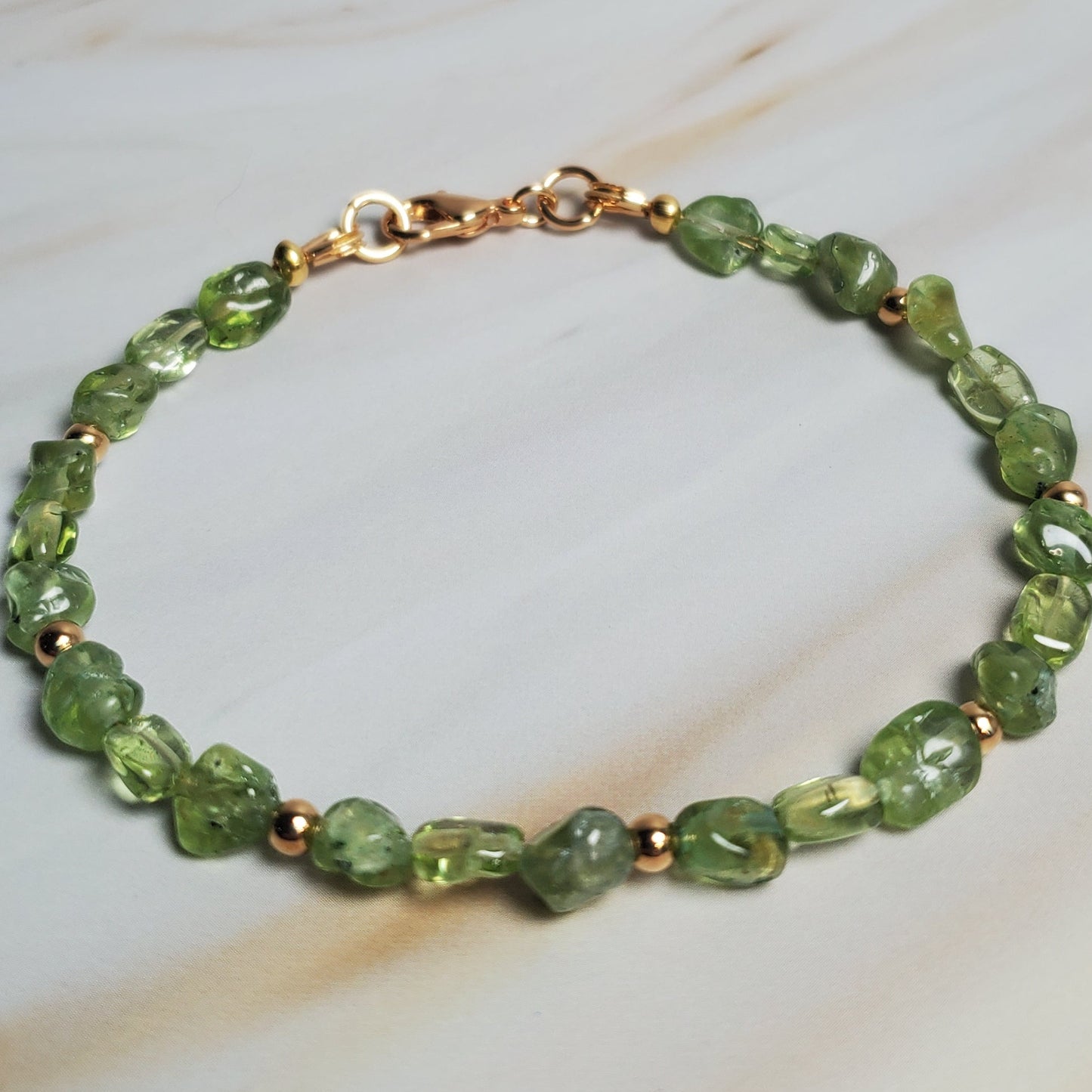 Green beaded bracelet with gold accents on a white fabric background