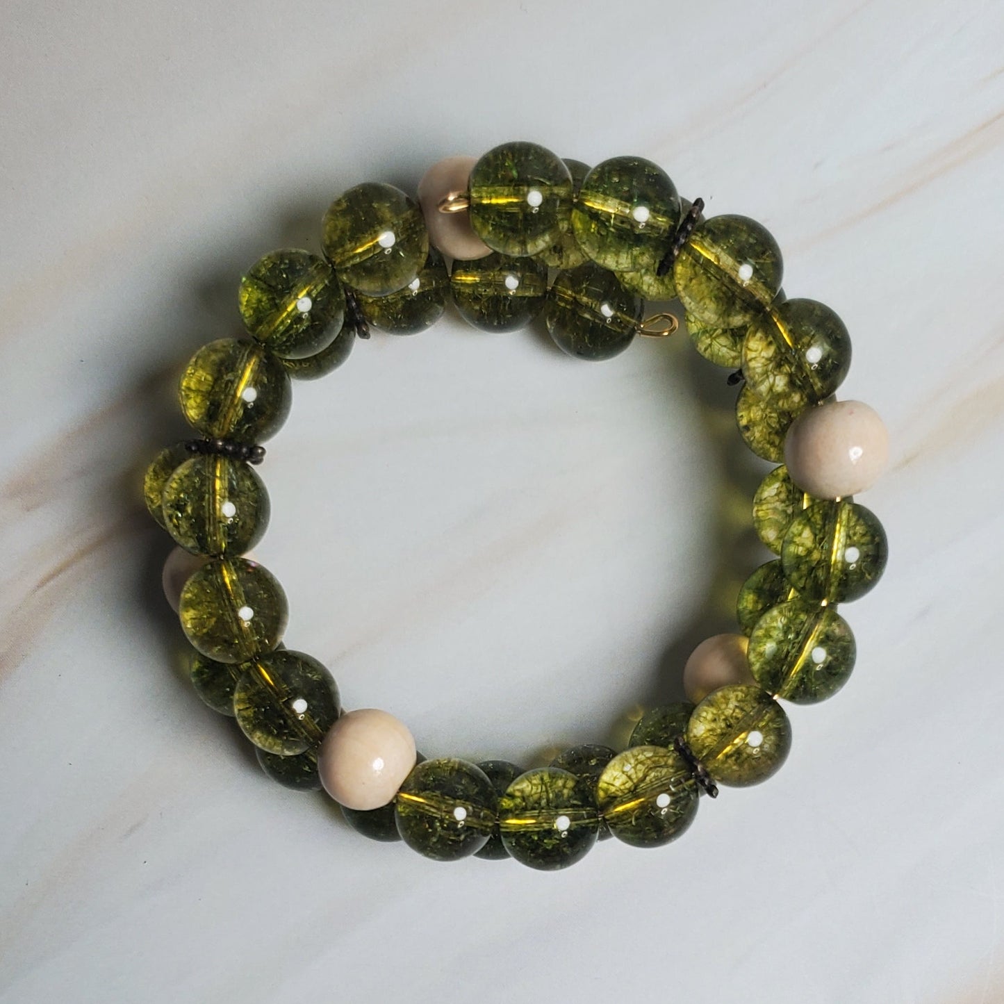 Green beaded bracelet with off-white beads on a marble surface