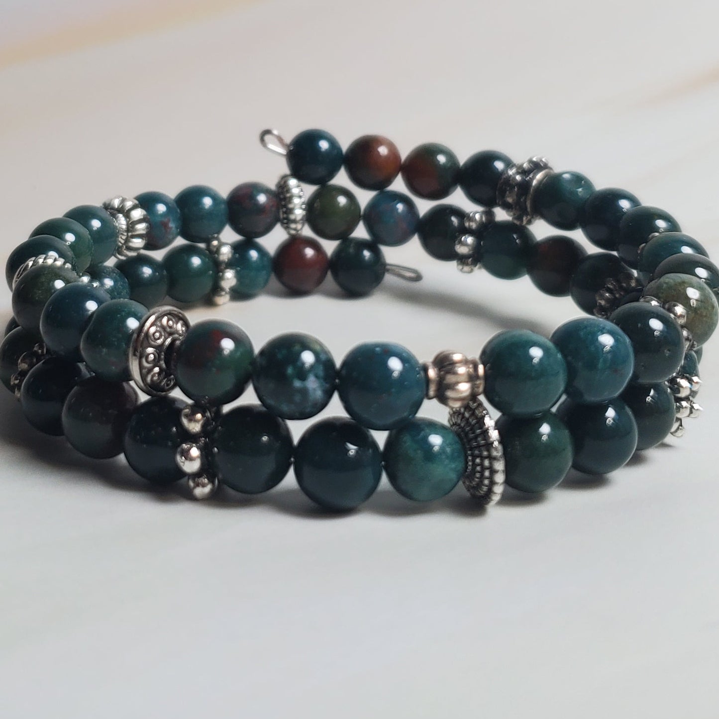 Stacked green beaded bracelet on a light wood surface