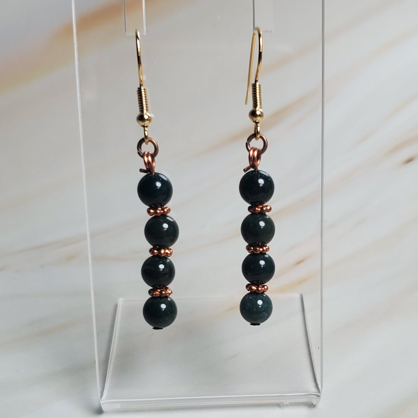 Green beaded earrings on a clear stand against a marble background