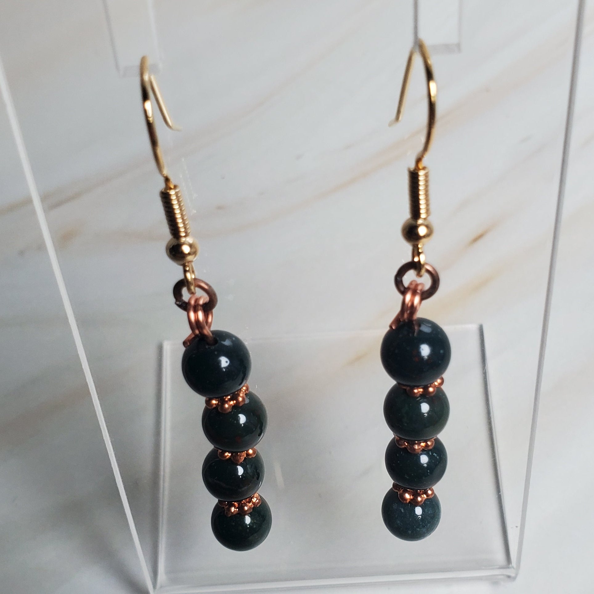 Green beaded earrings on a clear stand against a light background