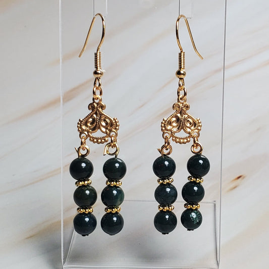 Dark Green beaded earrings on a clear stand against a marble background