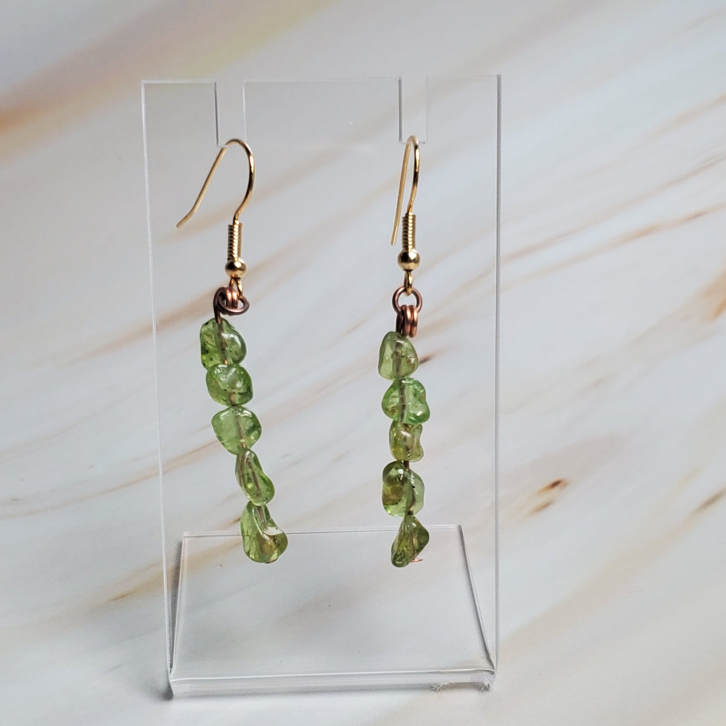 Green beaded earrings on a clear stand against a marble background