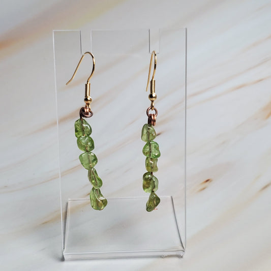Green beaded earrings on a clear stand against a marble background