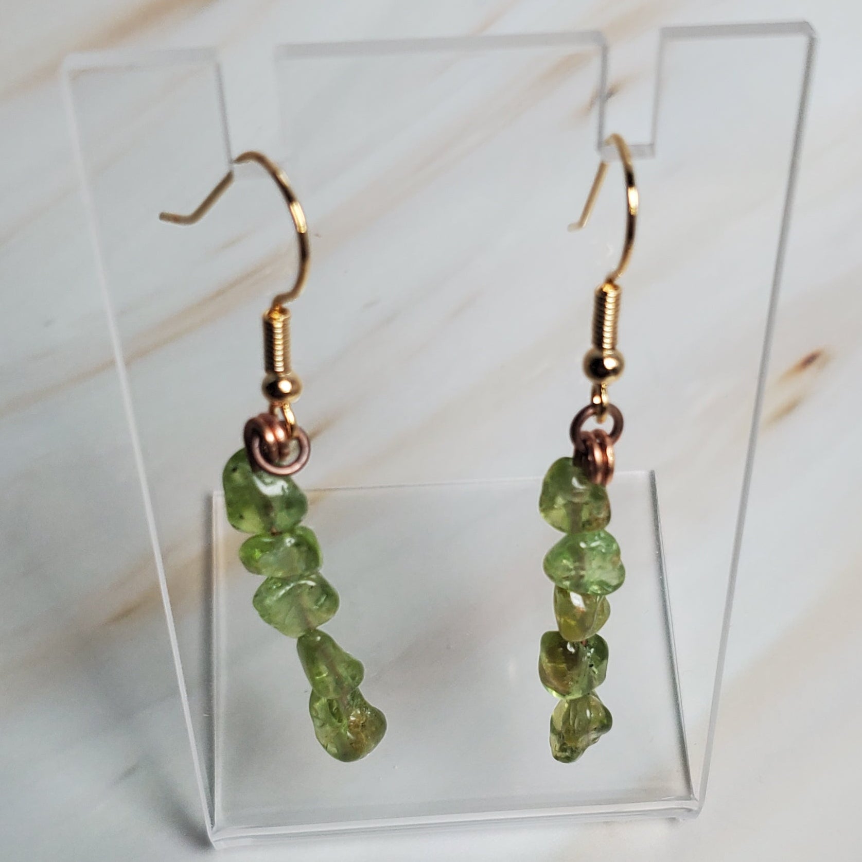 Green beaded earrings on a clear stand against a marble background