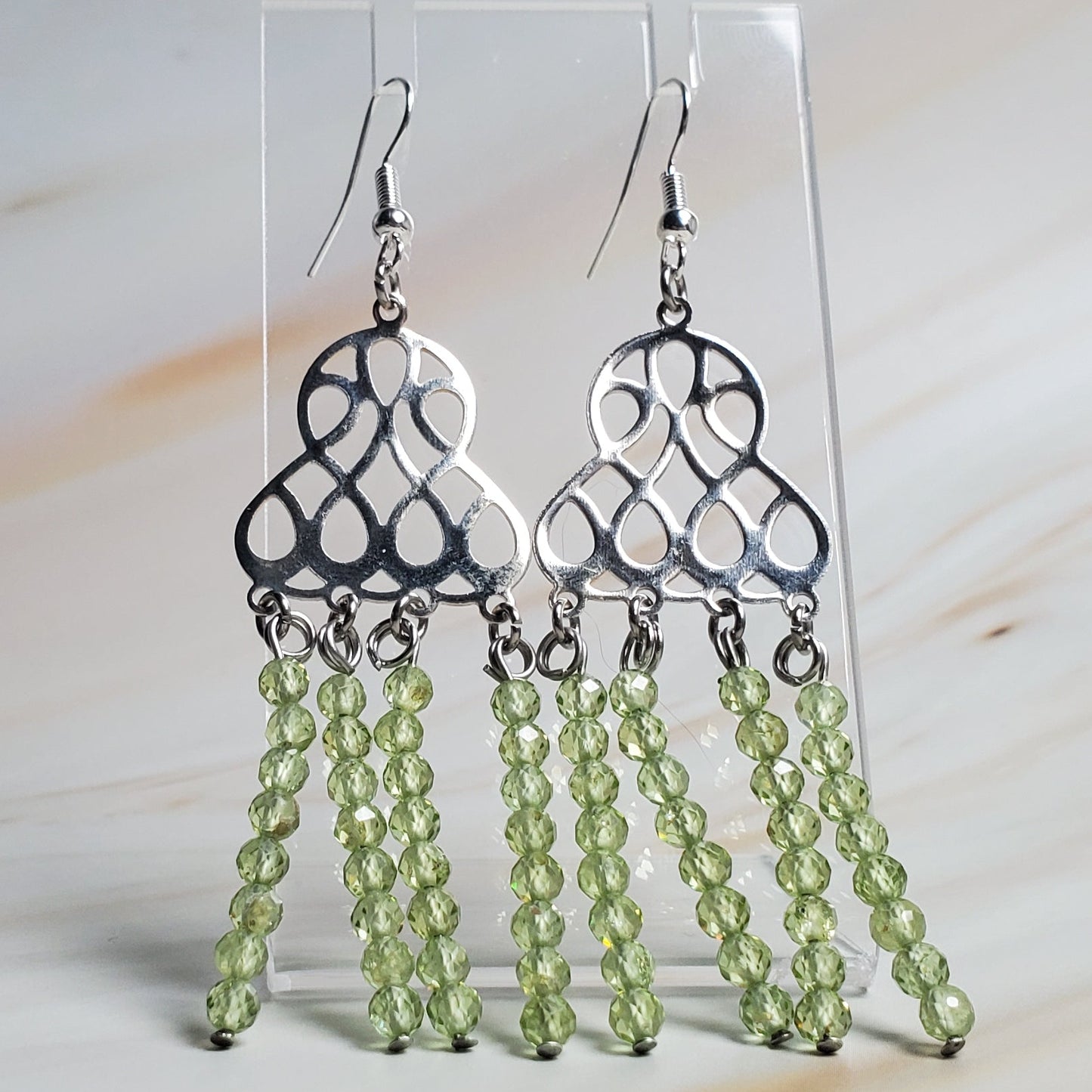 Silver chandelier earrings with green beads on a marble surface