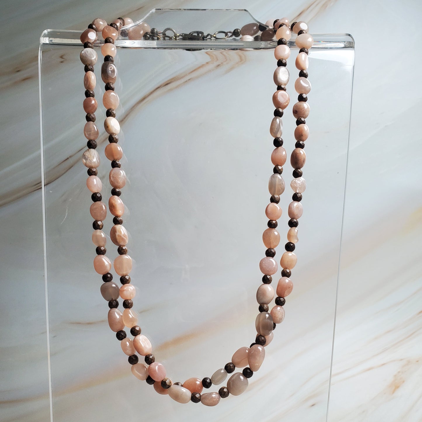 Beaded necklace on a clear stand against a marble background