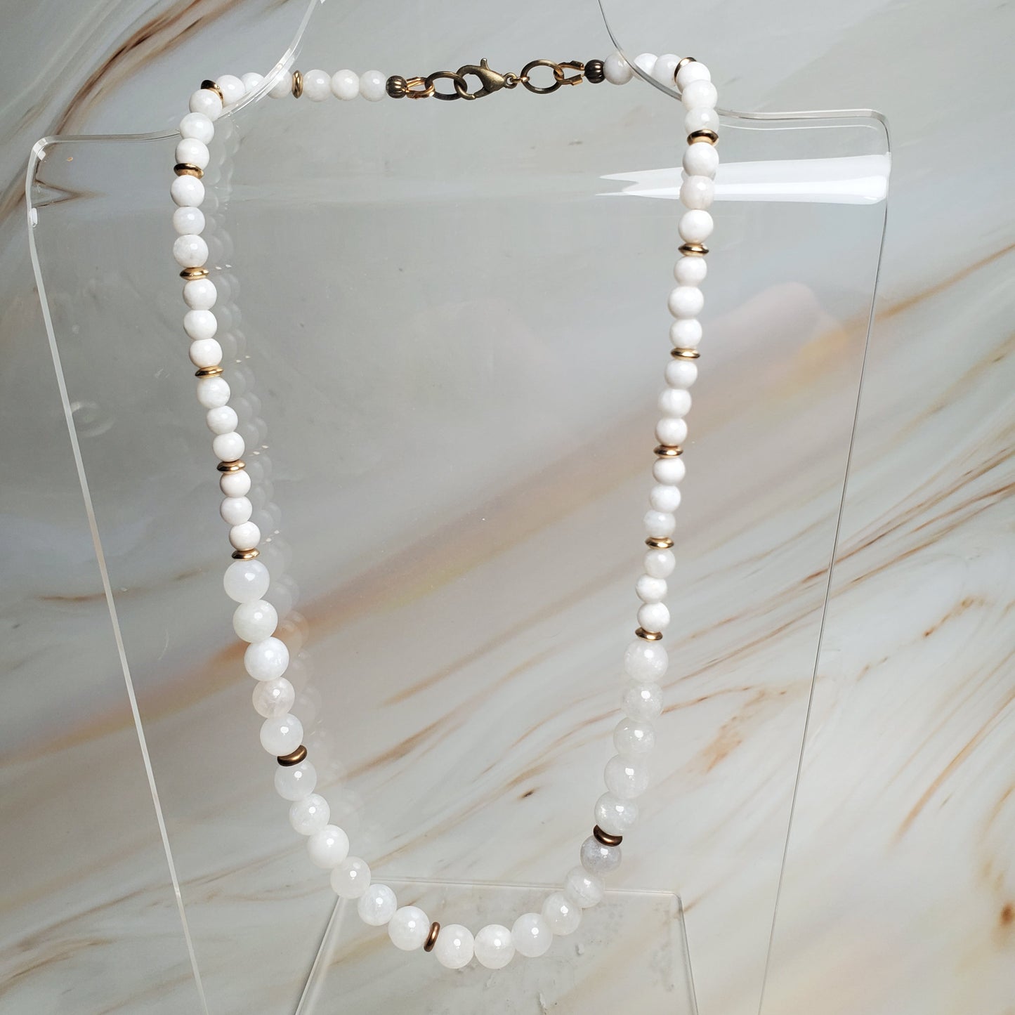 Moonstone necklace on a clear stand against a marble background
