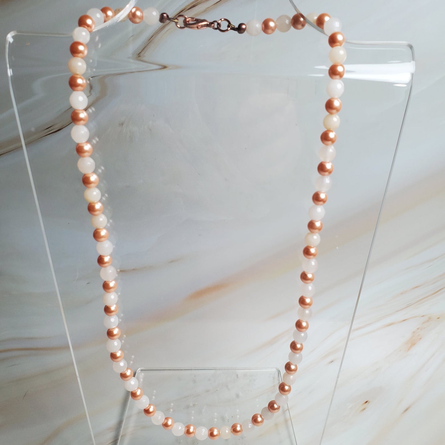 Pearl necklace on a clear stand against a marble background