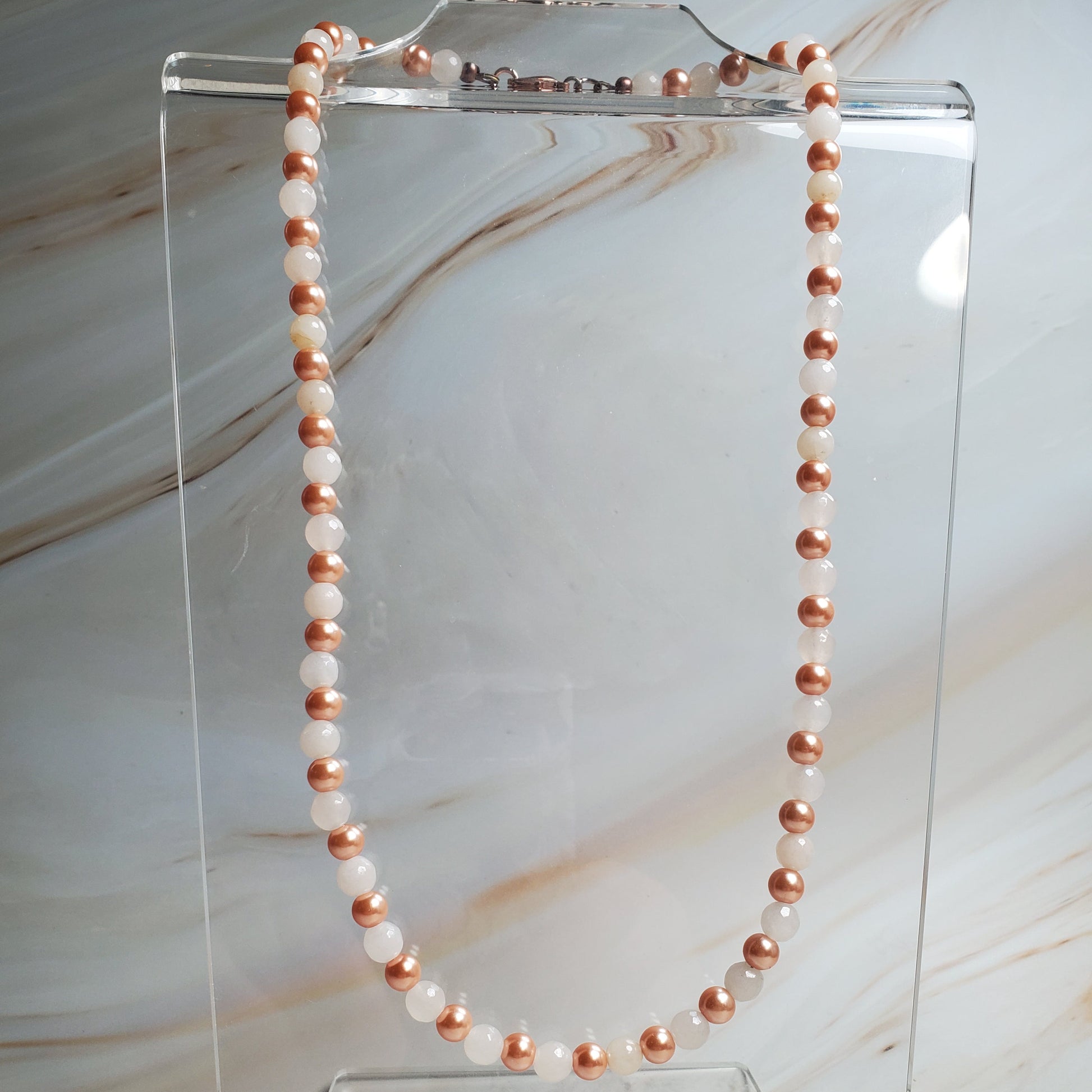 Necklace with rose gold and white beads on a clear stand against a marble background
