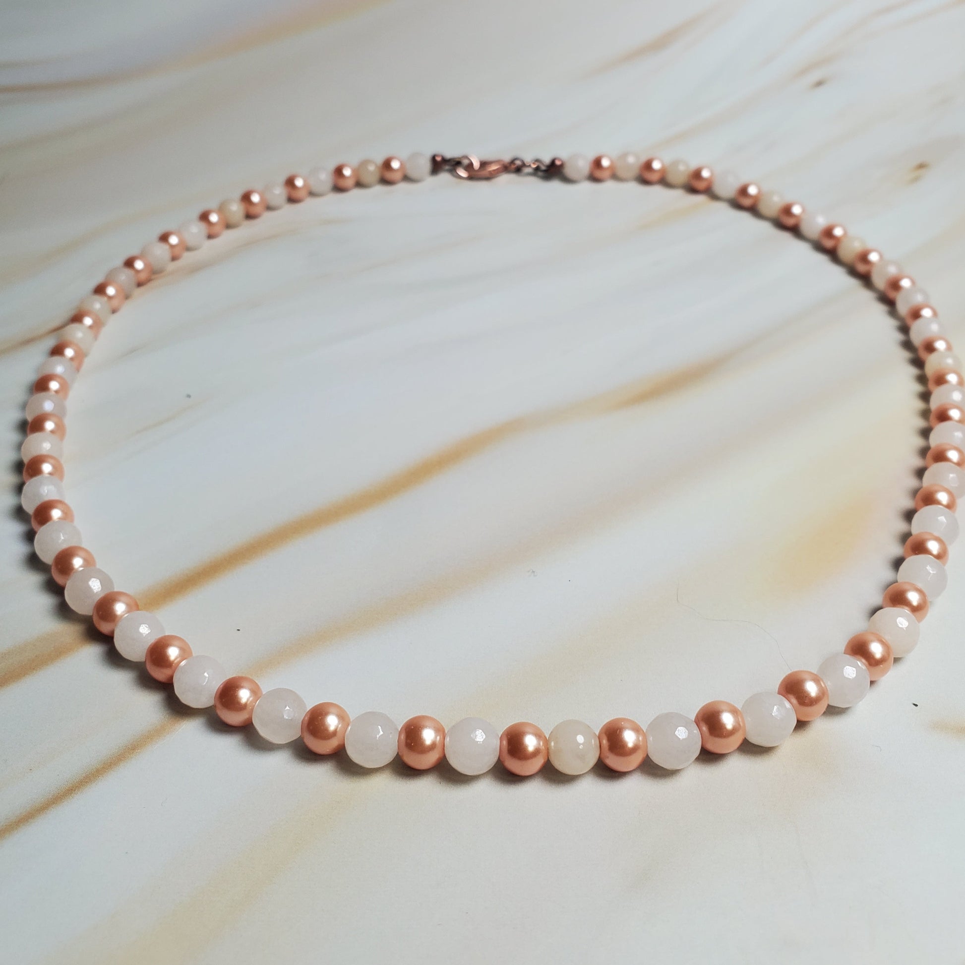 Necklace with rose gold and white beads on a marble surface