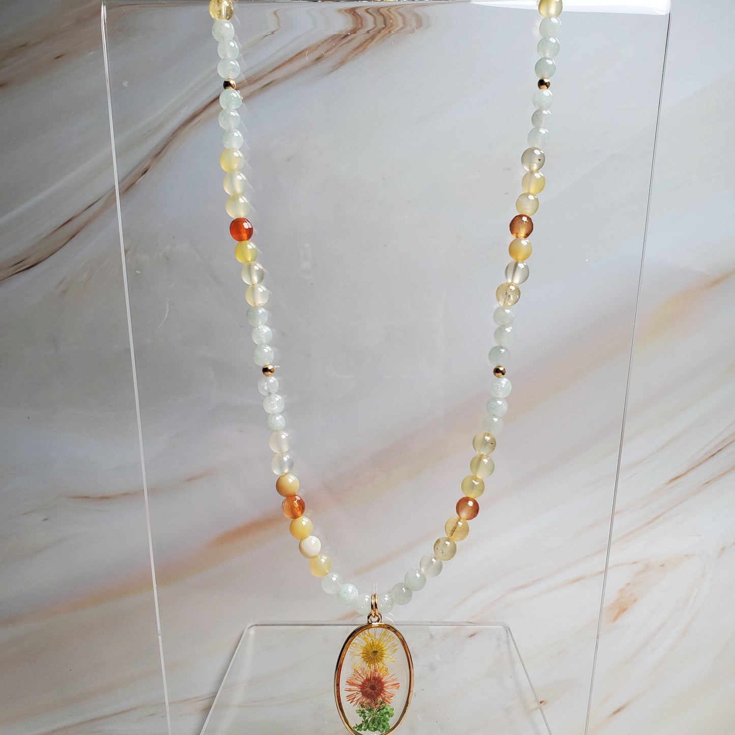 Necklace with a floral pendant on a clear stand against a marble background