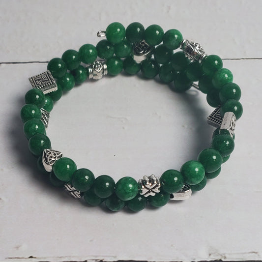 Green beaded bracelet with silver charms on a white wooden surface