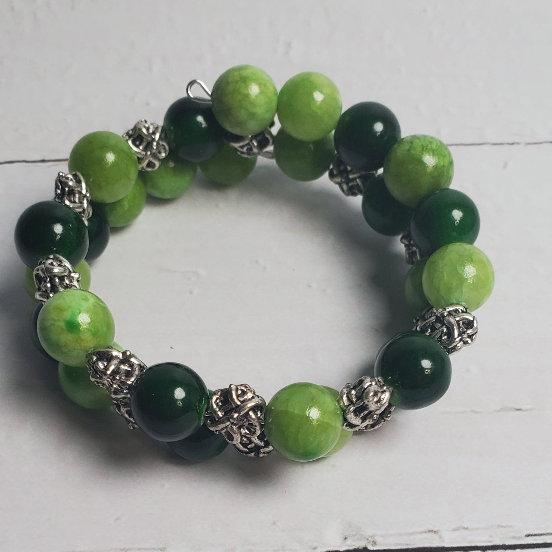Green beaded bracelet with silver accents on a white wooden surface