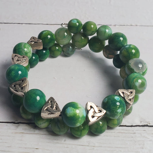 Green beaded bracelet with Celtic knot charms on a light wooden surface