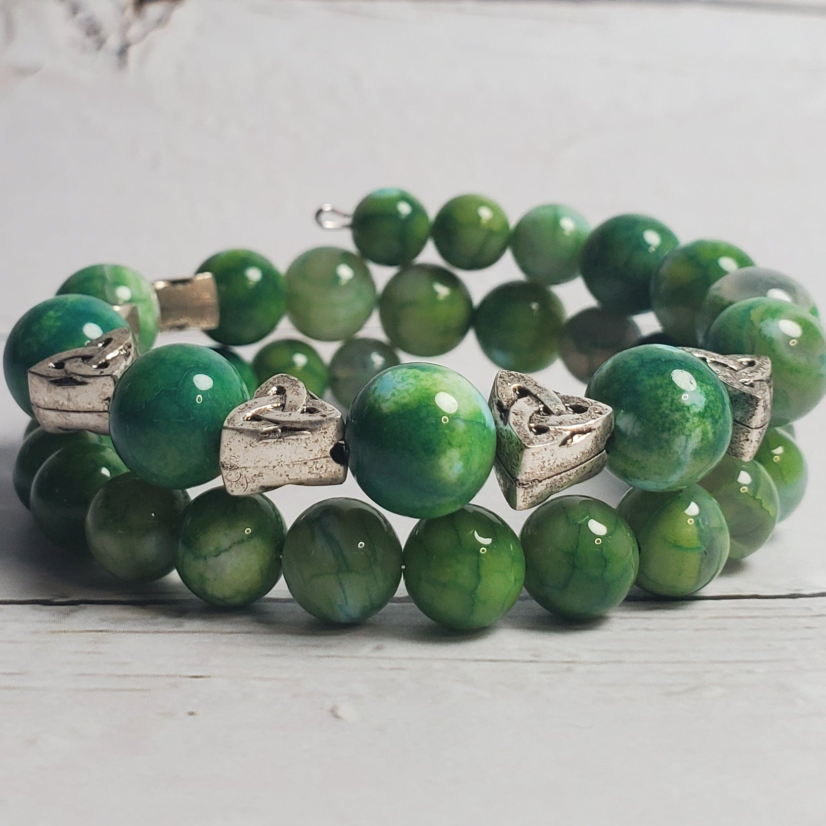 Green beaded bracelet with silver accents on a light wooden surface