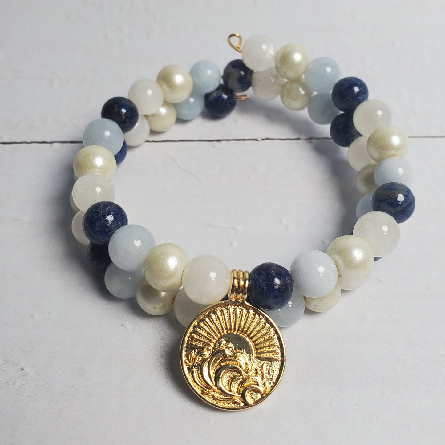 Beaded bracelet with a gold charm on a white wooden surface