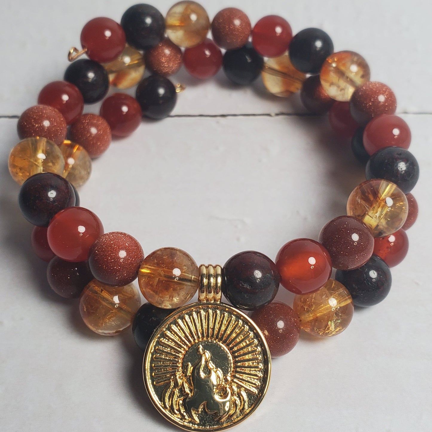 Beaded bracelet with a gold charm on a white wooden surface