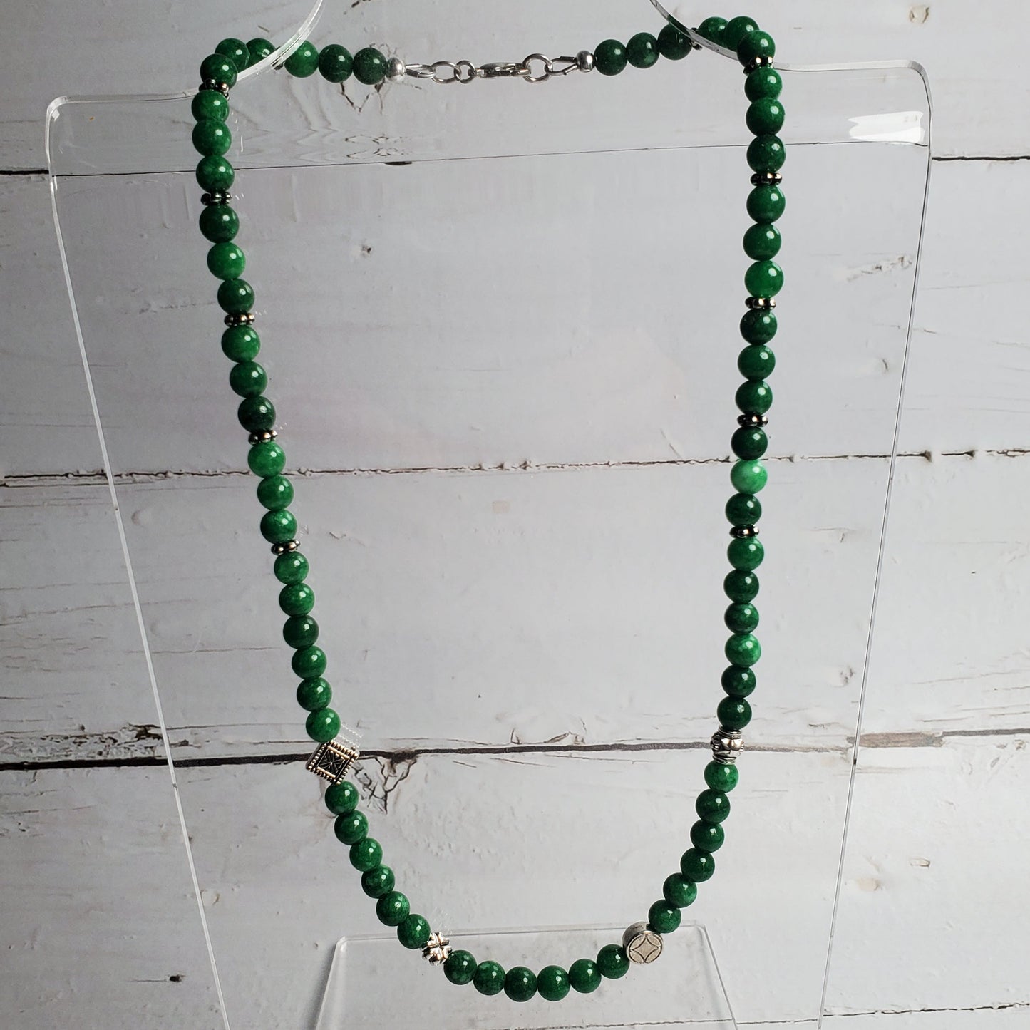 Green beaded necklace on a clear stand against a wooden background