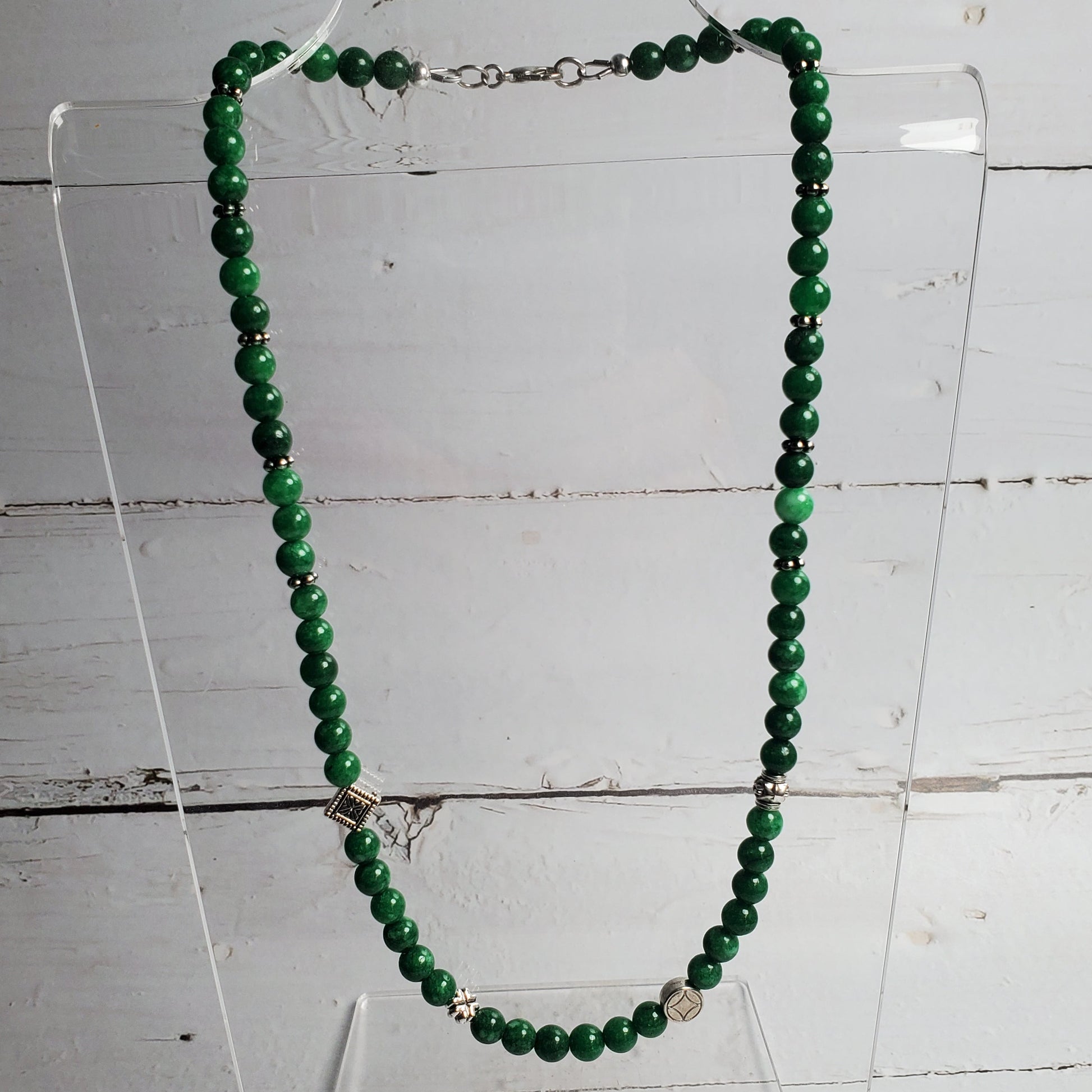 Green beaded necklace on a clear stand against a wooden background