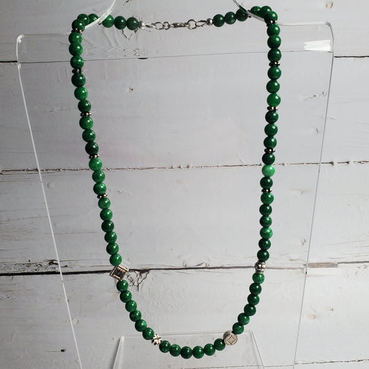 Green beaded necklace on a clear stand against a wooden background