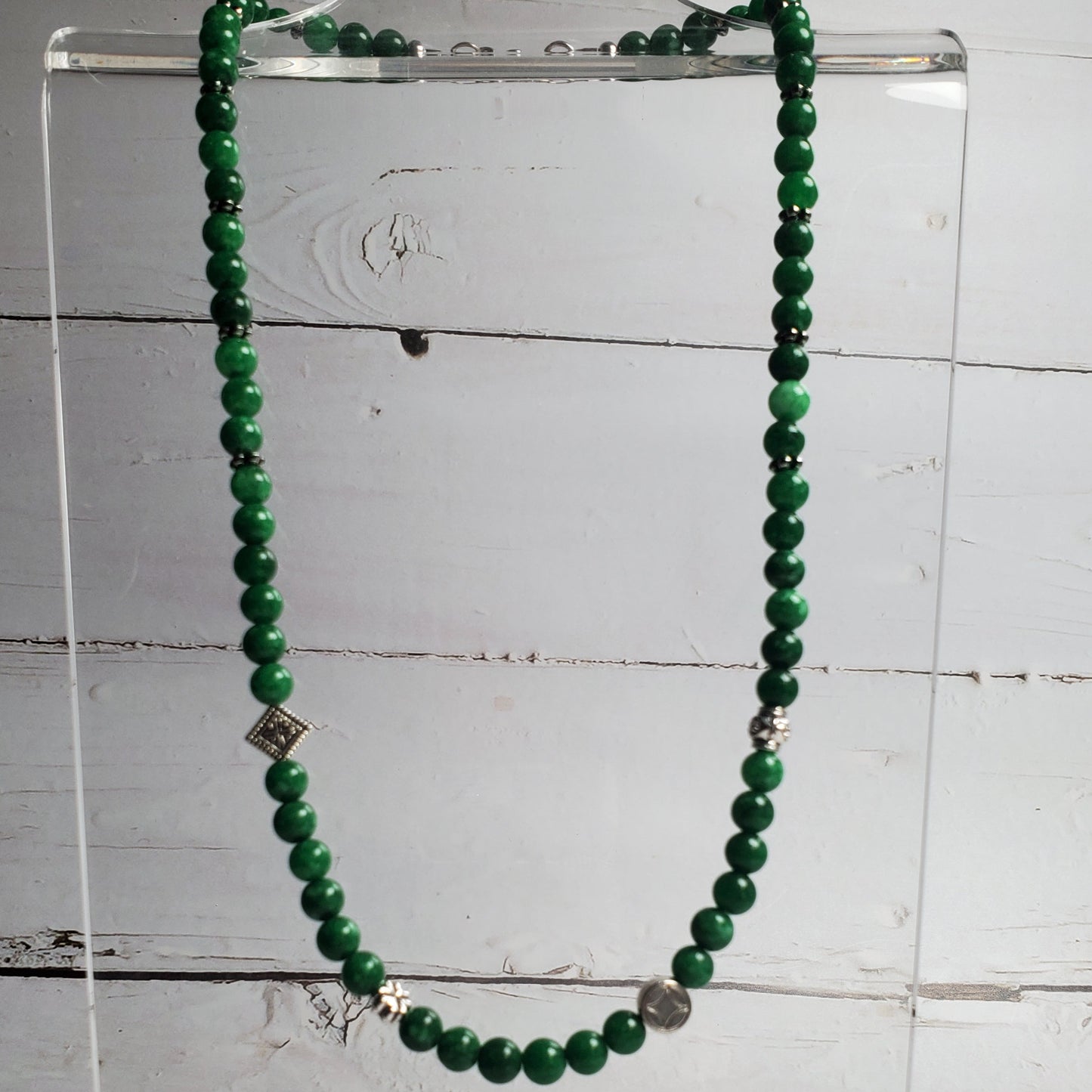 Green beaded necklace on a clear stand against a white wooden background