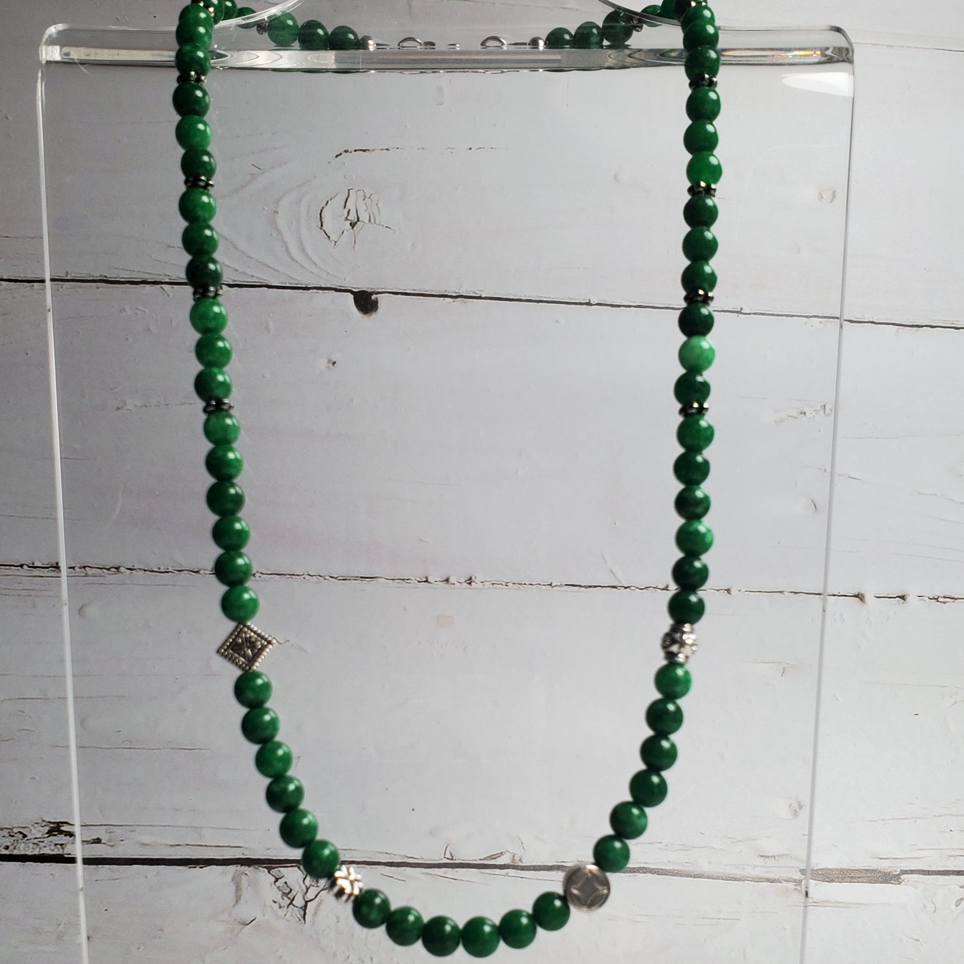 Green beaded necklace on a clear stand against a white wooden background