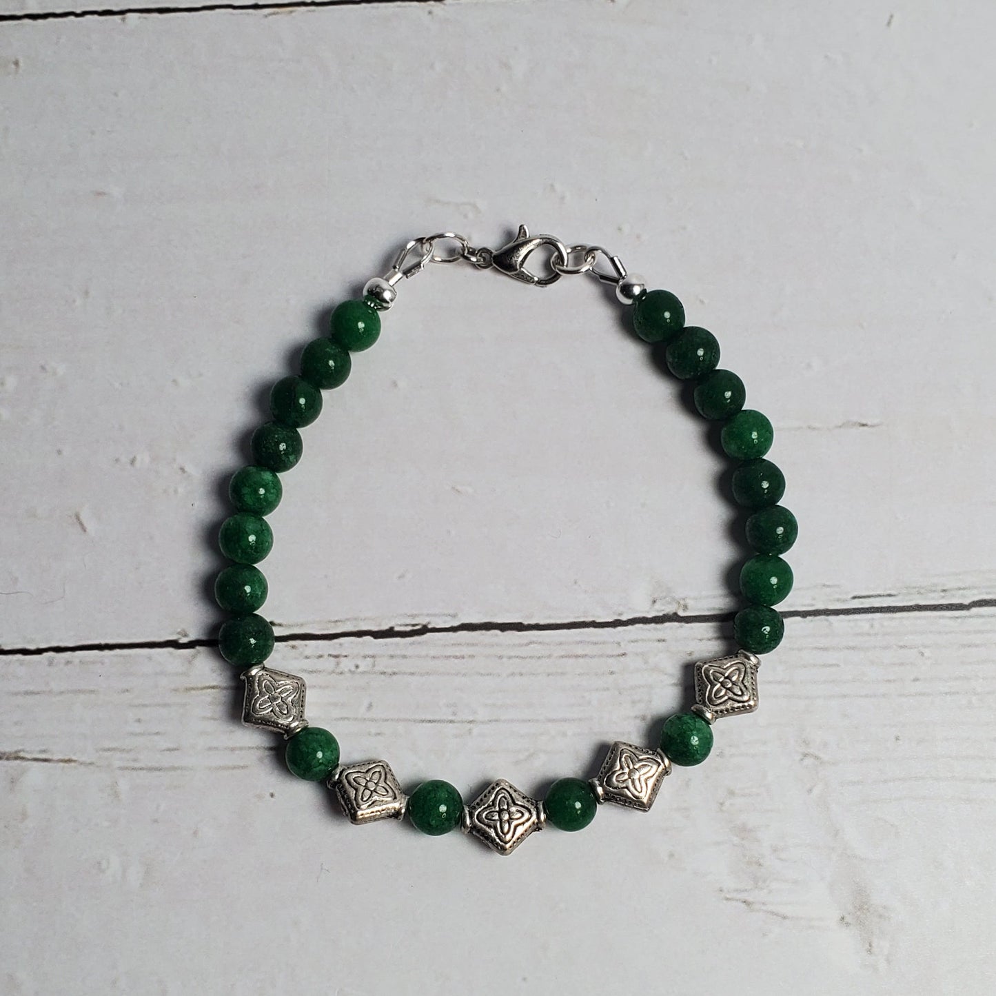 Green beaded bracelet with silver accents on a white wooden surface